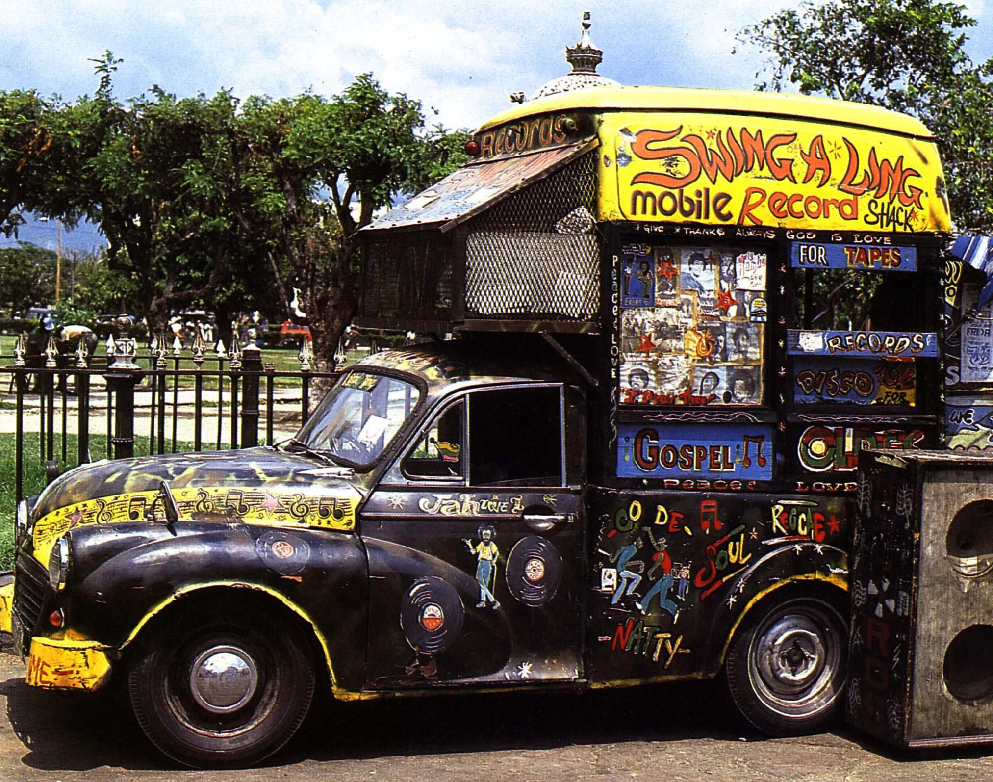 The iconic Swing-A-Ling Mobile Record Shack, a brightly decorated vehicle operated by Charlie Ace, parked on a street in Kingston, Jamaica, surrounded by vibrant music-themed artwork.