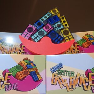 The Sound System Balance Game set, showing colorful balancing pieces on the red platform with packaging in the background.