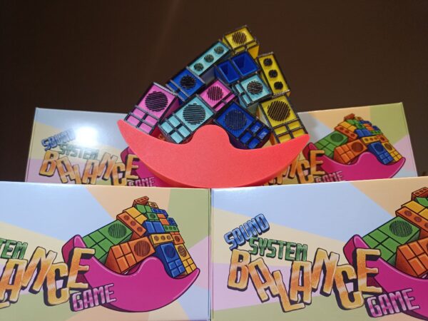 The Sound System Balance Game set, showing colorful balancing pieces on the red platform with packaging in the background.